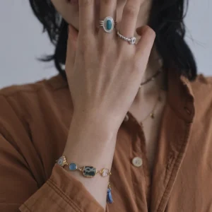 December Birthstone Ring-Natural Turquoise Ring in Sterling Silver 06 Close-up of hand near face wearing sterling silver rings, including a December Birthstone Ring with natural turquoise, styled with a gold bracelet featuring blue and green stones.