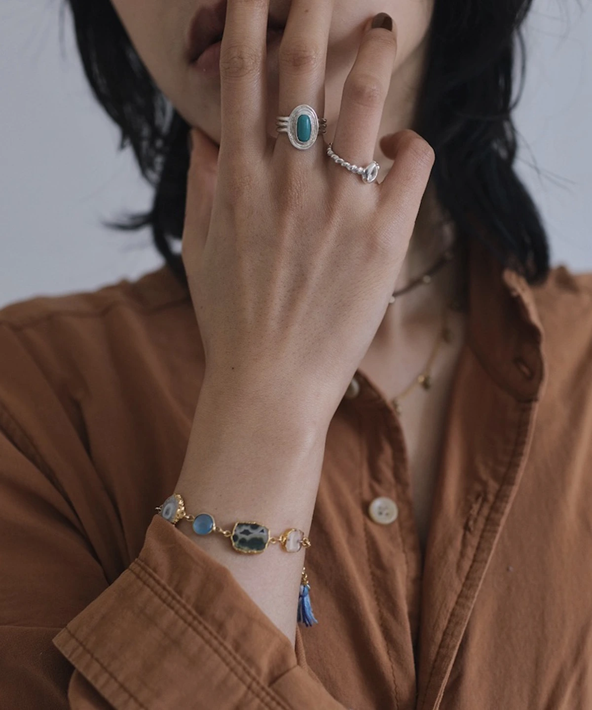 December Birthstone Ring-Natural Turquoise Ring in Sterling Silver 06 Close-up of hand near face wearing sterling silver rings, including a December Birthstone Ring with natural turquoise, styled with a gold bracelet featuring blue and green stones.