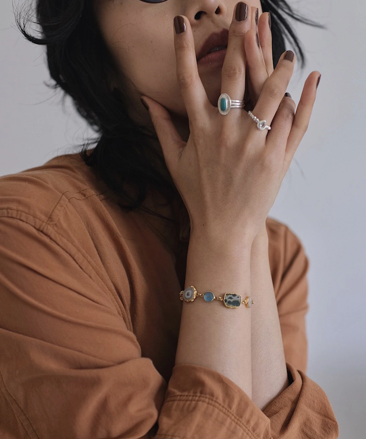December Birthstone Ring-Natural Turquoise Ring in Sterling Silver 08 Close-up of hands near face wearing sterling silver rings, including a December Birthstone Ring with natural turquoise, styled with a gold bracelet featuring blue and green stones.