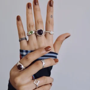 February Birthstone Ring-Natural Amethyst Ring in Sterling Silver 02 Two hands with brown nails wearing multiple silver rings, including a February Birthstone Ring with heart-shaped natural amethyst, styled with teardrop, sunburst, and geometric accents.