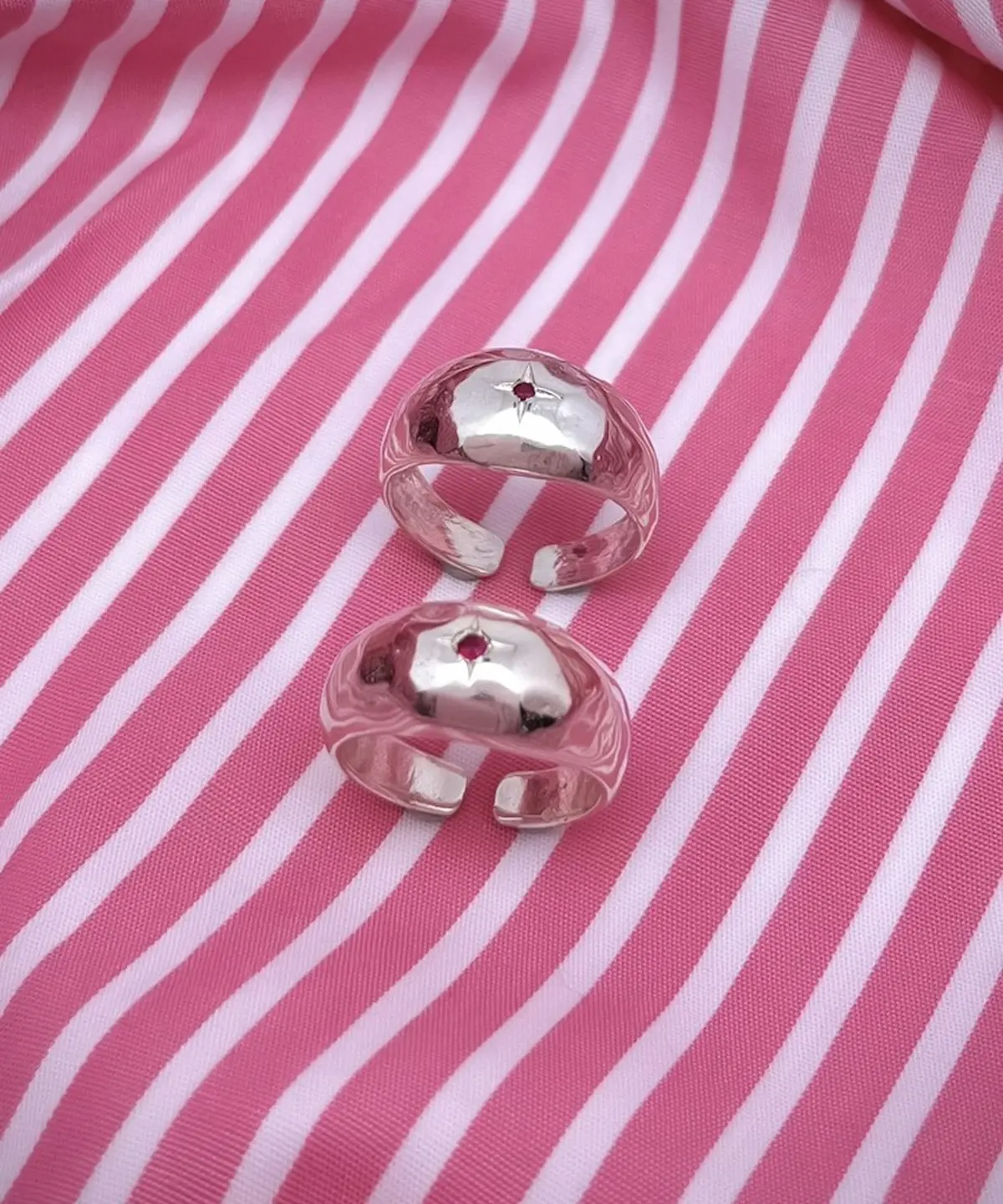 Two open-ended silver rings with hammered texture and red star-shaped natural ruby gemstones, placed on pink-striped fabric to showcase the July Birthstone Ring’s artisanal charm.