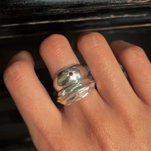 Hand wearing two silver rings on the middle finger, including a July Birthstone Ring with a red star-shaped natural ruby, styled against a dark textured background.