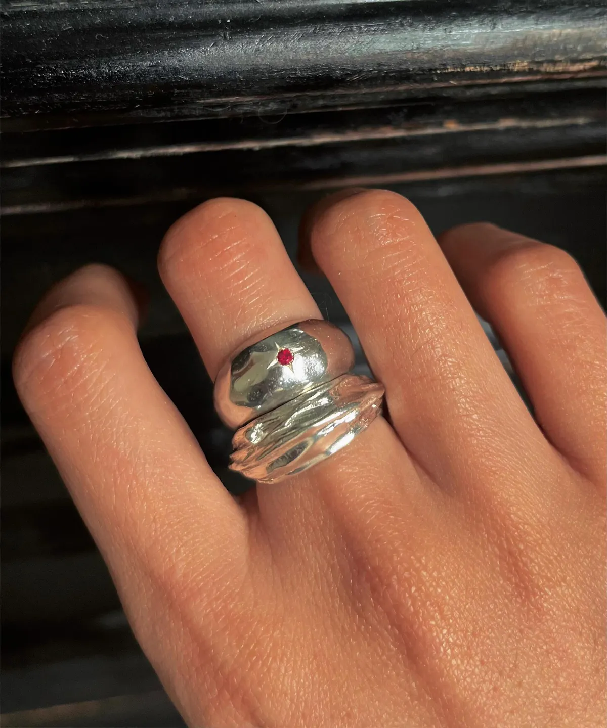 Hand wearing two silver rings on the middle finger, including a July Birthstone Ring with a red star-shaped natural ruby, styled against a dark textured background.