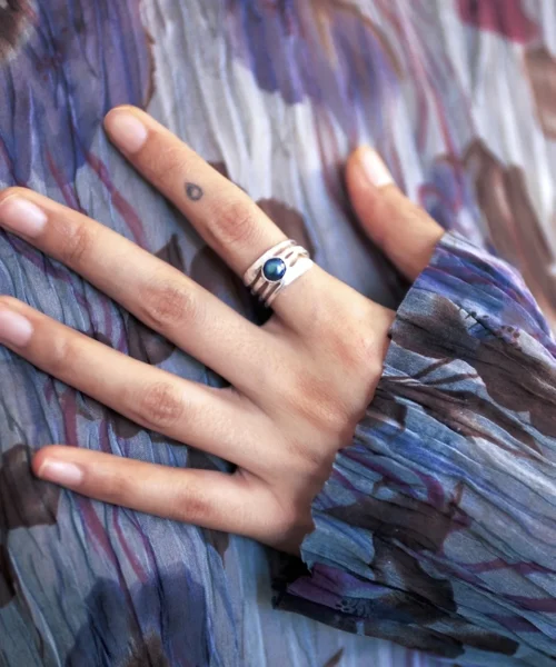 Close-up of a hand wearing a June Birthstone Ring with natural black pearl set in a sculptural sterling silver band; elegant Black Pearl Ring paired with patterned fabric and minimalist tattoo, highlighting handcrafted Silver Ring artistry.
