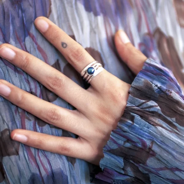 June Birthstone Ring-Natural Black Pearl Ring in Sterling Silver 01 Close-up of a hand wearing a June Birthstone Ring with natural black pearl set in a sculptural sterling silver band; elegant Black Pearl Ring paired with patterned fabric and minimalist tattoo, highlighting handcrafted Silver Ring artistry.