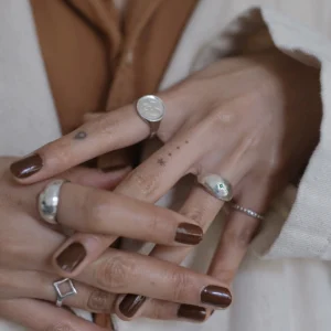 A hand styled with multiple silver rings, including a delicate May Birthstone Ring featuring a small natural emerald gem. Perfect for layering, this minimalist Natural Emerald Ring adds subtle green elegance to any stack.