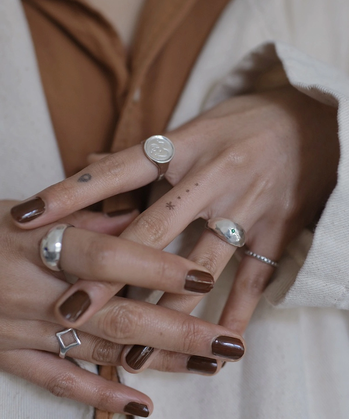 A hand styled with multiple silver rings, including a delicate May Birthstone Ring featuring a small natural emerald gem. Perfect for layering, this minimalist Natural Emerald Ring adds subtle green elegance to any stack.
