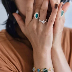 Close-up of hands adorned with silver rings and a gold-toned bracelet, featuring a November Birthstone Ring with topaz, styled with dark nails and earthy tones for an artisanal, elegant look.