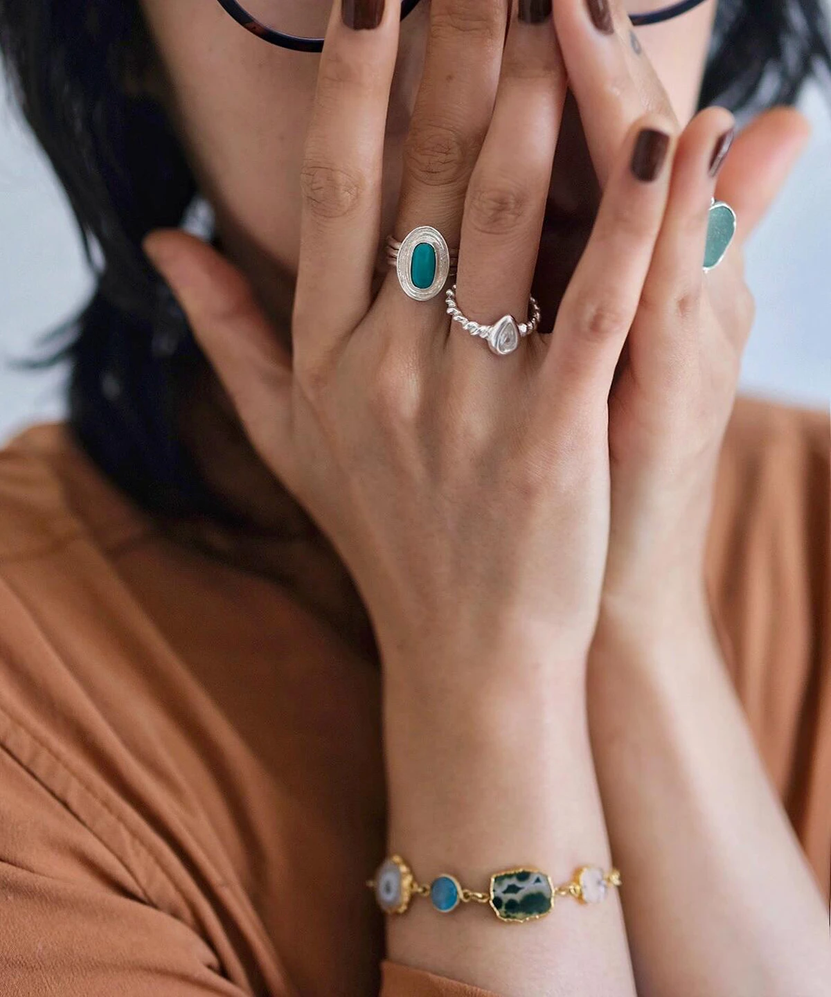 Close-up of hands adorned with silver rings and a gold-toned bracelet, featuring a November Birthstone Ring with topaz, styled with dark nails and earthy tones for an artisanal, elegant look.