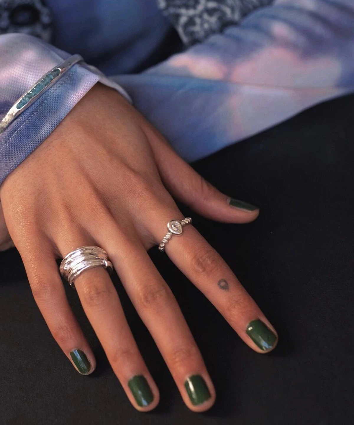 Hand with green nails wearing two sterling silver rings, including a November Birthstone Ring with topaz and beaded band, styled with heart tattoo and blue gemstone bracelet.