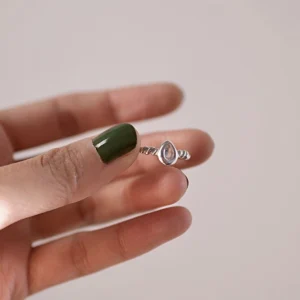 Close-up of hand holding a sterling silver November Birthstone Ring with topaz, featuring a twisted band and teardrop gemstone, styled with green nails and soft lighting.