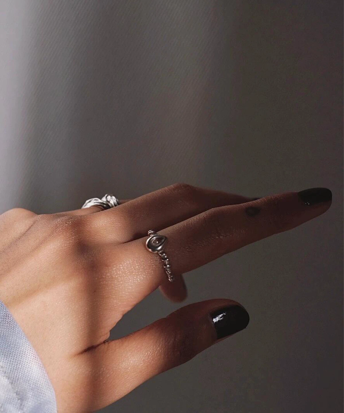 Hand with dark nails wearing sterling silver rings, including a twisted band November Birthstone Ring with topaz, styled in soft lighting to highlight texture and elegance.