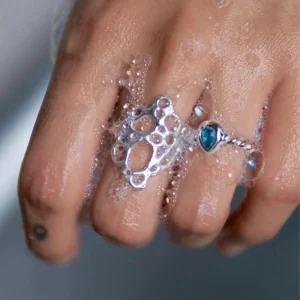 Hand covered in soap bubbles wearing sterling silver rings, including a November Birthstone Ring with topaz, styled with a circular tattoo and bubble-inspired textures.