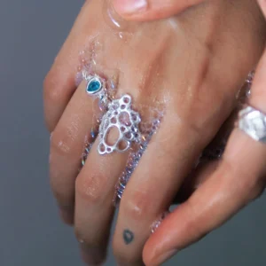 Hand covered in soap bubbles wearing sterling silver rings, including a November Birthstone Ring with topaz, styled with a blue gemstone and delicate tattoo for ethereal charm.