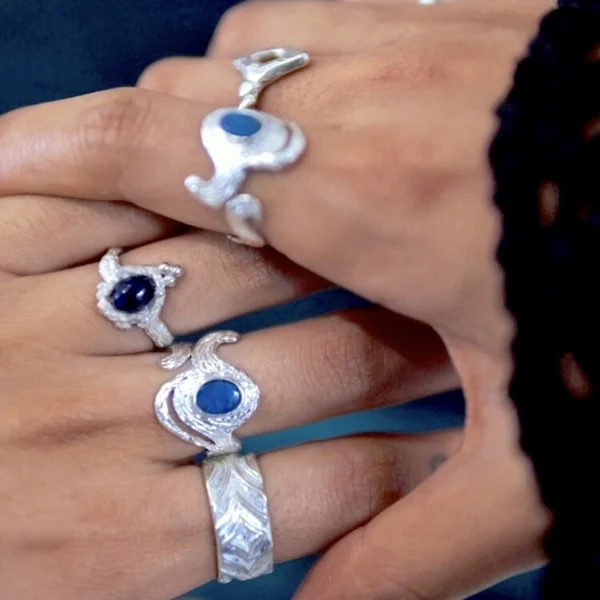 Two hands adorned with intricately designed Silver Rings featuring natural black opals; elegant October Birthstone Ring styles with deep blue stones and sculptural bands, showcasing artistic Black Opal Ring craftsmanship and sterling silver detail.