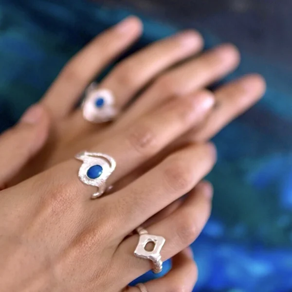 October Birthstone Ring-Natural Black Opal Ring in Sterling Silver 03 Two hands adorned with multiple Silver Rings, including October Birthstone Rings with natural black opals; elegant Black Opal Ring designs with sculptural bands and deep blue stones, showcasing handcrafted sterling silver artistry and cosmic-inspired styling.