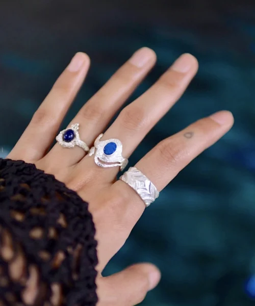 Close-up of a hand wearing multiple Silver Rings, including October Birthstone Rings with natural black opals; elegant Black Opal Ring designs with sculptural bands and deep blue stones, highlighting handcrafted sterling silver artistry and personal style.