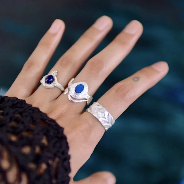 Close-up of a hand wearing multiple Silver Rings, including October Birthstone Rings with natural black opals; elegant Black Opal Ring designs with sculptural bands and deep blue stones, highlighting handcrafted sterling silver artistry and personal style.