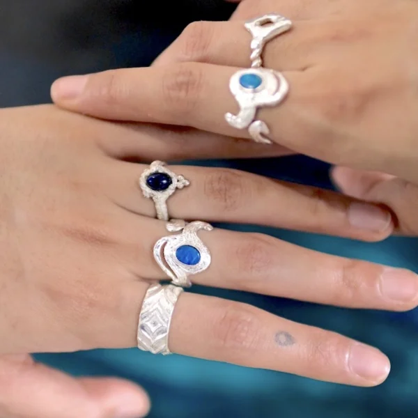 October Birthstone Ring-Natural Black Opal Ring in Sterling Silver 07 Two hands adorned with multiple Silver Rings, including October Birthstone Rings with natural black opals; elegant Black Opal Ring designs with sculptural bands and deep blue stones, showcasing handcrafted sterling silver artistry and expressive styling.
