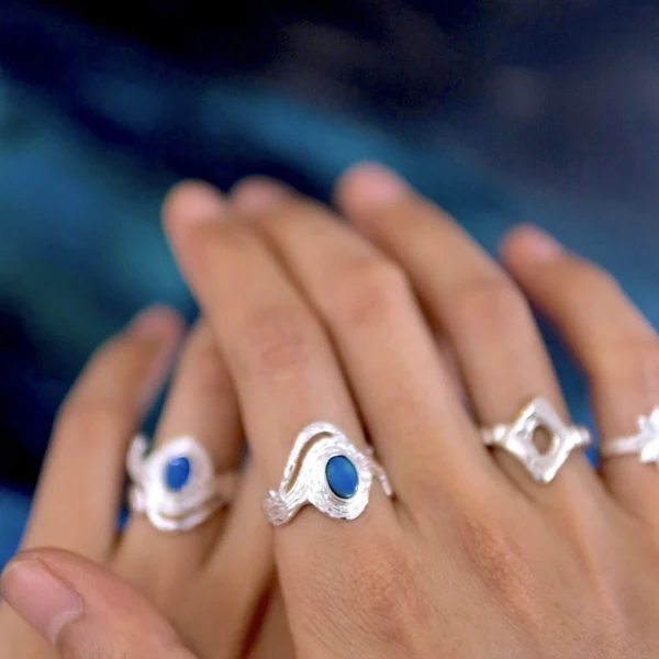 Two hands adorned with multiple Silver Rings, including October Birthstone Rings with natural black opals; elegant Black Opal Ring designs with sculptural bands and deep blue stones, showcasing handcrafted sterling silver artistry and personal style.
