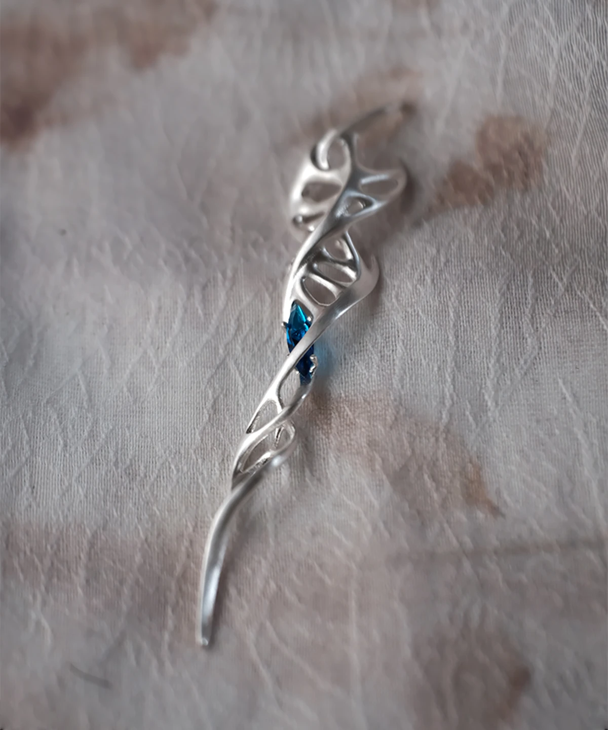 Close-up of Lazesoul Handmade S925 Sterling Silver Spiral Pendant Necklace on fabric background. The spiral pendant features flowing vine-like silver curves with loops and a deep blue gemstone at the center, highlighting the artistry of this elegant spiral necklace.