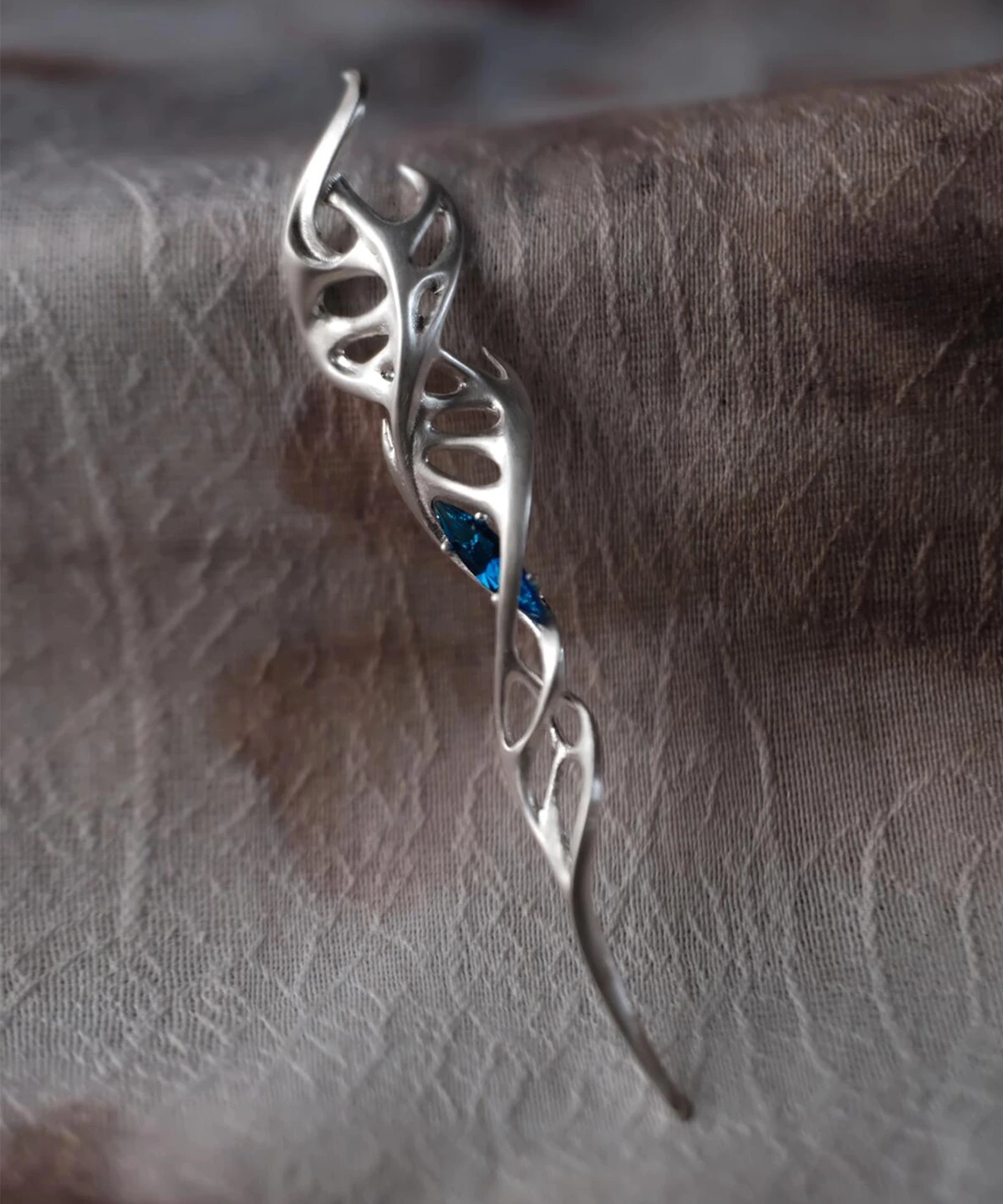 Close-up of Lazesoul Handmade S925 Sterling Silver Spiral Pendant Necklace placed on textured fabric. The spiral pendant features flowing silver curves with vine-like twists and embedded blue gemstones, highlighting the refined artistry of this elegant spiral necklace.