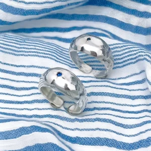 Two sterling silver open-ended rings with hammered texture and small natural sapphire gemstones, placed on striped fabric to showcase the September Birthstone Ring’s artisanal charm.