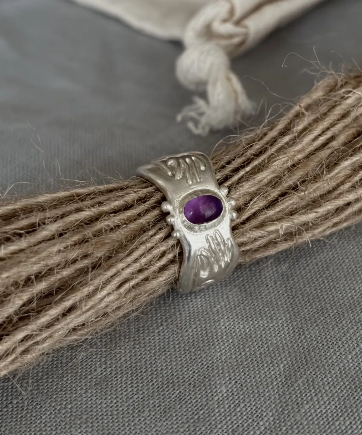 999 Silver Ring with central oval Natural Amethyst gemstone and engraved cosmic-inspired details, styled around natural twine with soft fabric background; a handcrafted Natural Amethyst Ring with celestial charm and artisanal texture.