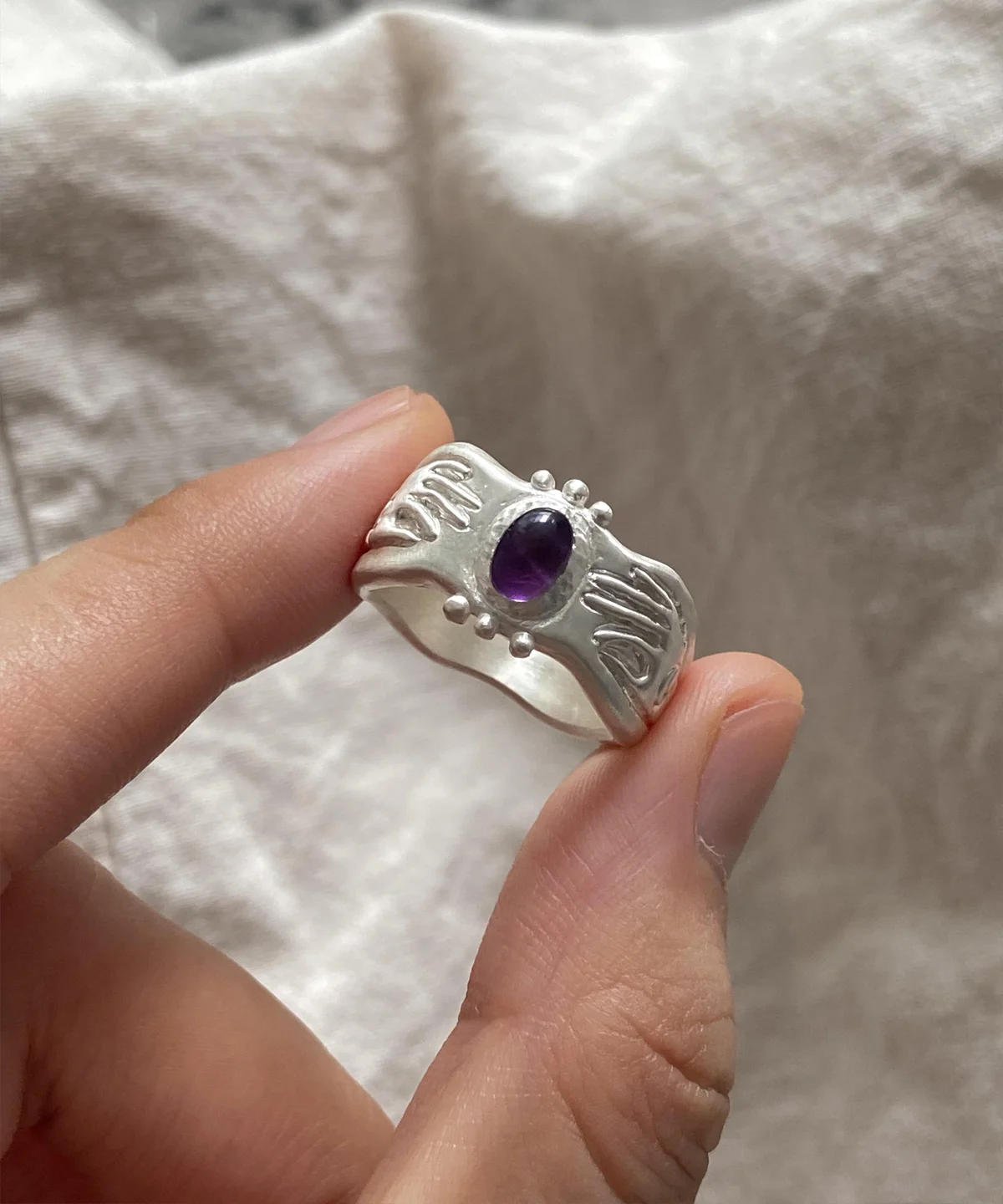 999 Silver Ring with deep purple Natural Amethyst gemstone and engraved crescent moon, eye, and cosmic symbols; a handcrafted Natural Amethyst Ring held between fingers, highlighting mystical design and artisanal craftsmanship.