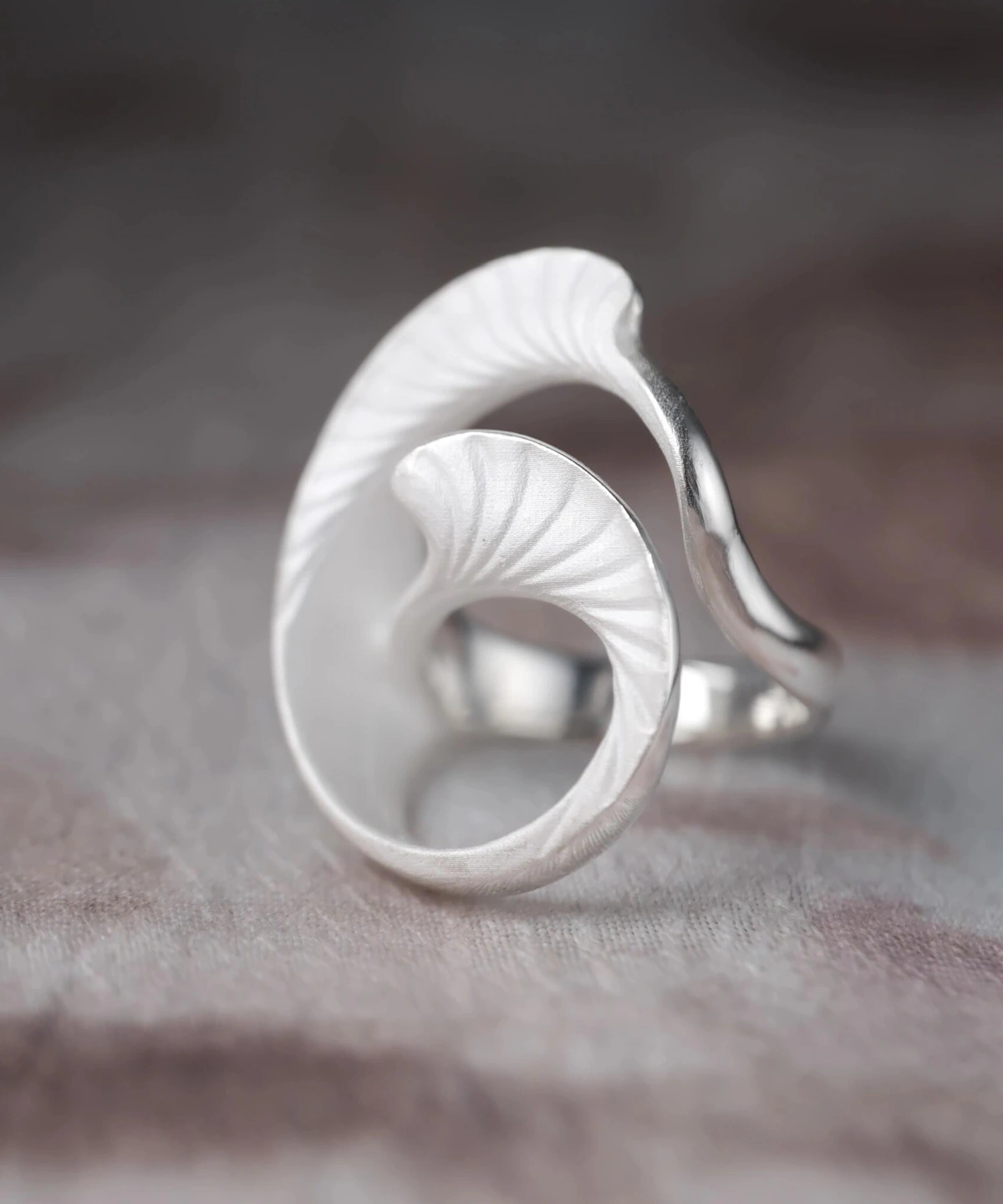 Arc Glow S925 Sterling Silver Ring with sculptural leaf-inspired design, featuring curved, textured elements and matte finish; a nature-inspired Unique Ring styled on hand against organic surface and dark background.