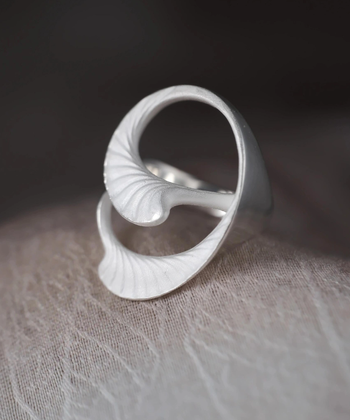 Arc Glow S925 Sterling Silver Ring with sculptural leaf-inspired design and matte vein-textured surface; a nature-inspired Unique Ring featuring intertwined curved forms, styled on a textured neutral background.