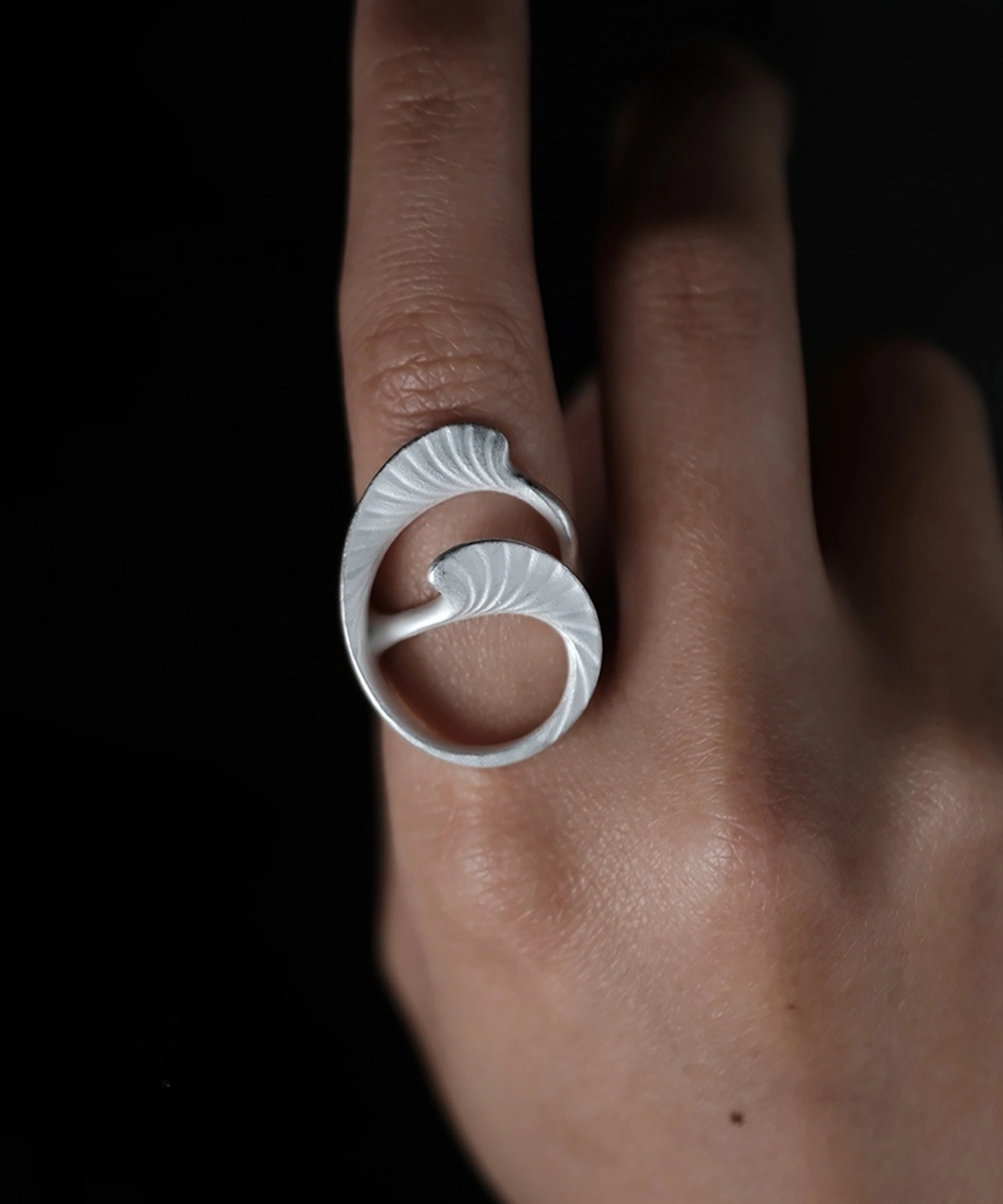 Arc Glow S925 Sterling Silver Ring with sculptural leaf-inspired design and radial vein texture; a nature-inspired Unique Ring featuring intertwined curved forms, worn on hand and styled against a dark organic surface.