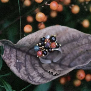 925 Sterling Silver Ring with multicolored Natural Stone beads in black, red, blue, and purple, accented with golden spheres and leaf charm; a handcrafted Silver Ring displayed on dried leaf with berry plant background.
