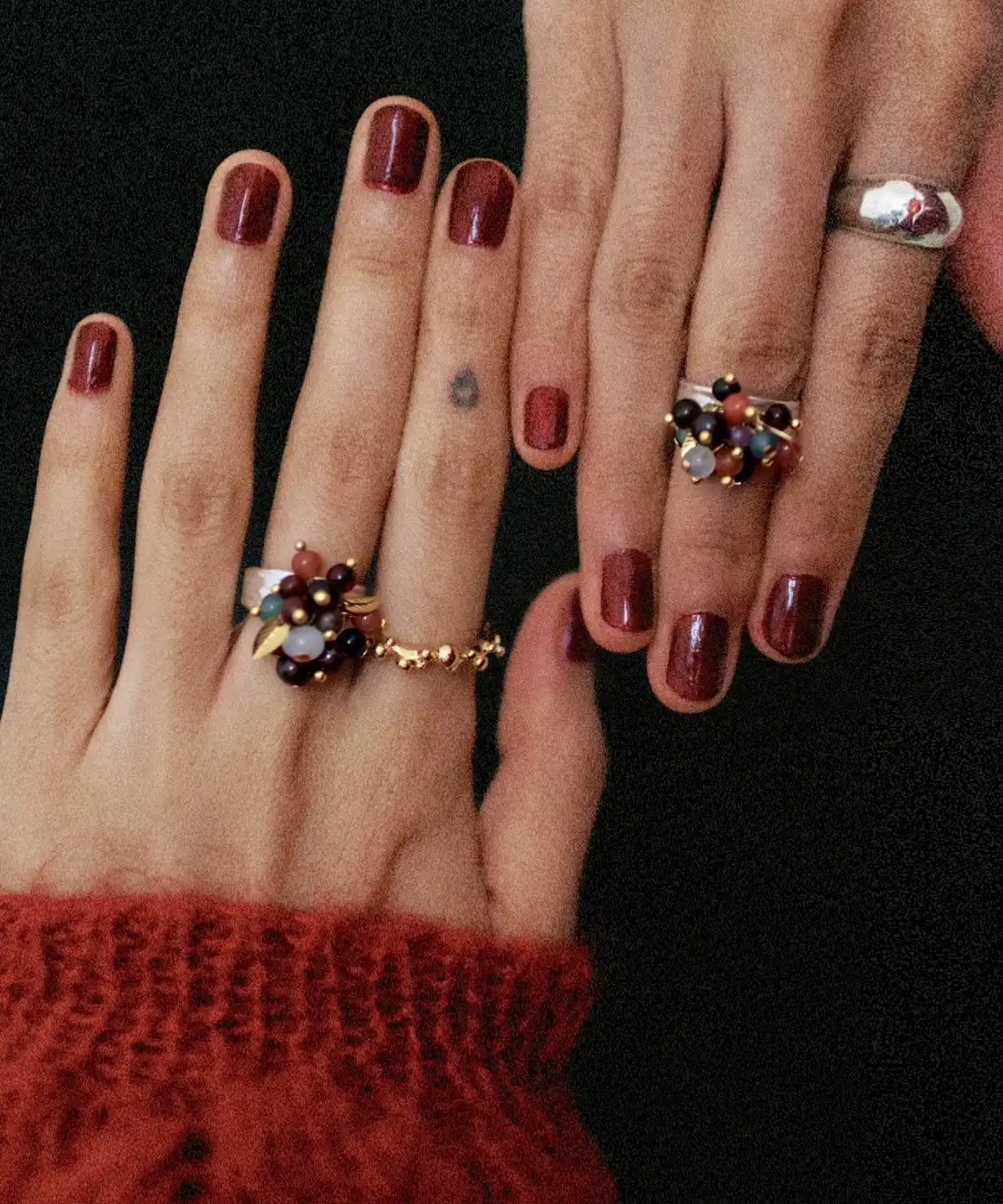 925 Sterling Silver Ring with multicolored Natural Stone beads in black, red, purple, and gold, worn on manicured hands with burgundy nails and paired with gold and silver bands; a handcrafted Silver Ring showcasing vibrant detail and artistic style.