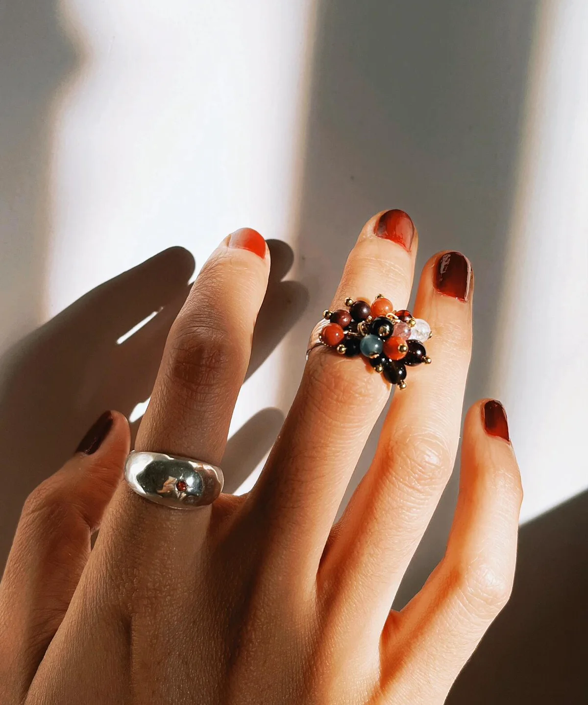 925 Sterling Silver Ring with multicolored Natural Stone beads in black, red, blue, and white, worn on hand with reddish-brown nails; a handcrafted Silver Ring with golden accents and floral-inspired design, styled in dramatic lighting.