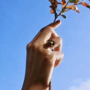 925 Sterling Silver Ring with multicolored Natural Stone beads in red, black, blue, and white, worn on hand holding a leafy branch against blue sky; a handcrafted Silver Ring with floral-inspired design and golden accents.