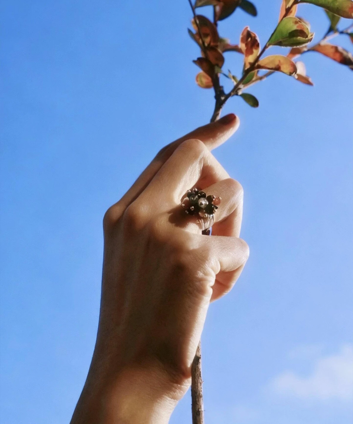 925 Sterling Silver Ring with multicolored Natural Stone beads in red, black, blue, and white, worn on hand holding a leafy branch against blue sky; a handcrafted Silver Ring with floral-inspired design and golden accents.