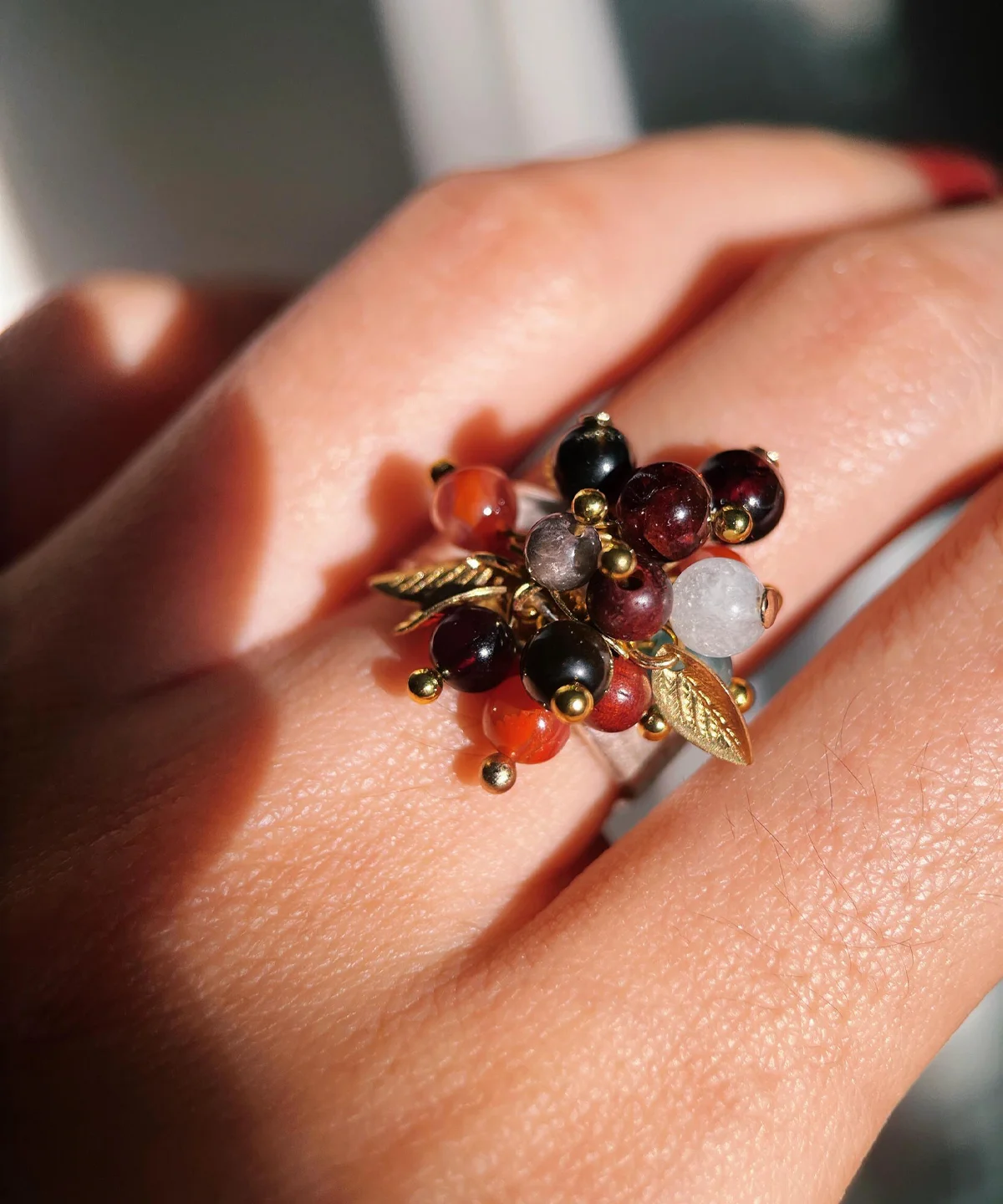 925 Sterling Silver Ring with multicolored Natural Stone beads in red, black, orange, and translucent white, accented with golden leaves and spheres; a handcrafted Silver Ring worn on hand in close-up view.