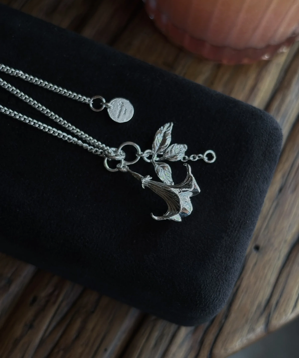 Handmade S925 Silver Necklace featuring a detailed datura flower pendant with sculpted petals and leaves, displayed on black velvet with custom disc charm; a botanical-inspired Flower Necklace with elegant craftsmanship.