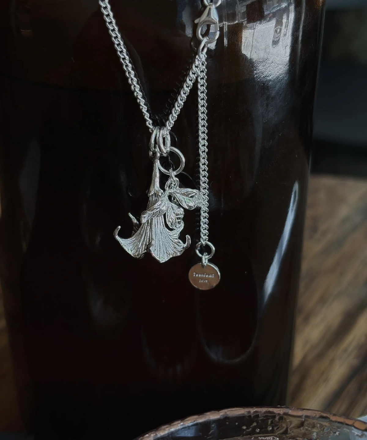 Datura Flower Necklace-Handmade S925 Silver With Custom Disc 05 Handmade S925 Silver Necklace with detailed datura flower pendant and custom disc tag, featuring petal and leaf engravings; a unique Flower Necklace displayed against a dark glossy surface for contrast and elegance.