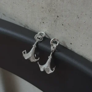 Datura-Handcrafted S925 Sterling Silver Flower Earrings 01 S925 Sterling Silver Datura Flower Earrings with sculptural petal-like curves and twisted loop detail; handcrafted Silver Earrings styled on black and gray surface with concrete wall backdrop, highlighting botanical elegance and artisanal design.