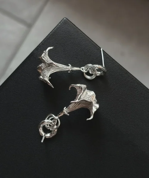 S925 Sterling Silver Datura Flower Earrings with sculptural petal-like forms and intertwined loops; handcrafted Silver Earrings styled on black textured surface, showcasing botanical elegance and artistic craftsmanship.