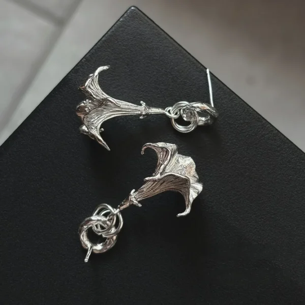 S925 Sterling Silver Datura Flower Earrings with sculptural petal-like forms and intertwined loops; handcrafted Silver Earrings styled on black textured surface, showcasing botanical elegance and artistic craftsmanship.