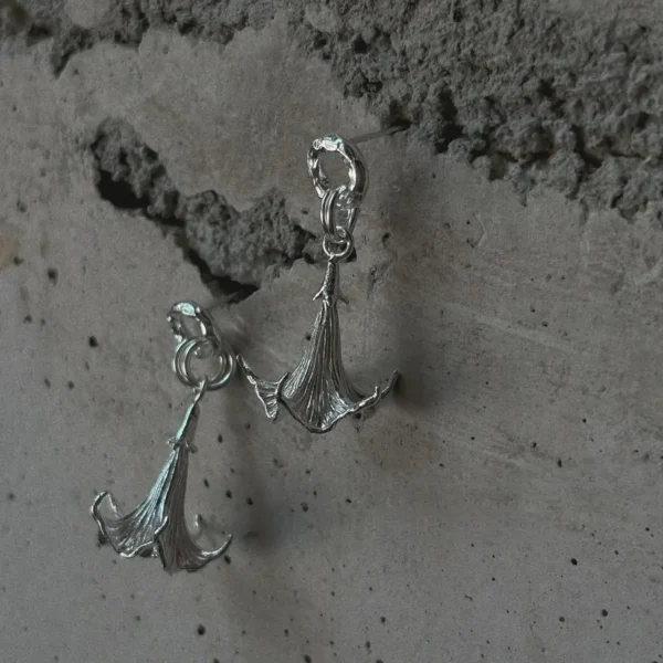 S925 Sterling Silver Datura Flower Earrings with sculptural, downward-facing blooms and textured petal details; handcrafted Silver Earrings styled against a rough concrete wall for contrast and elegance.