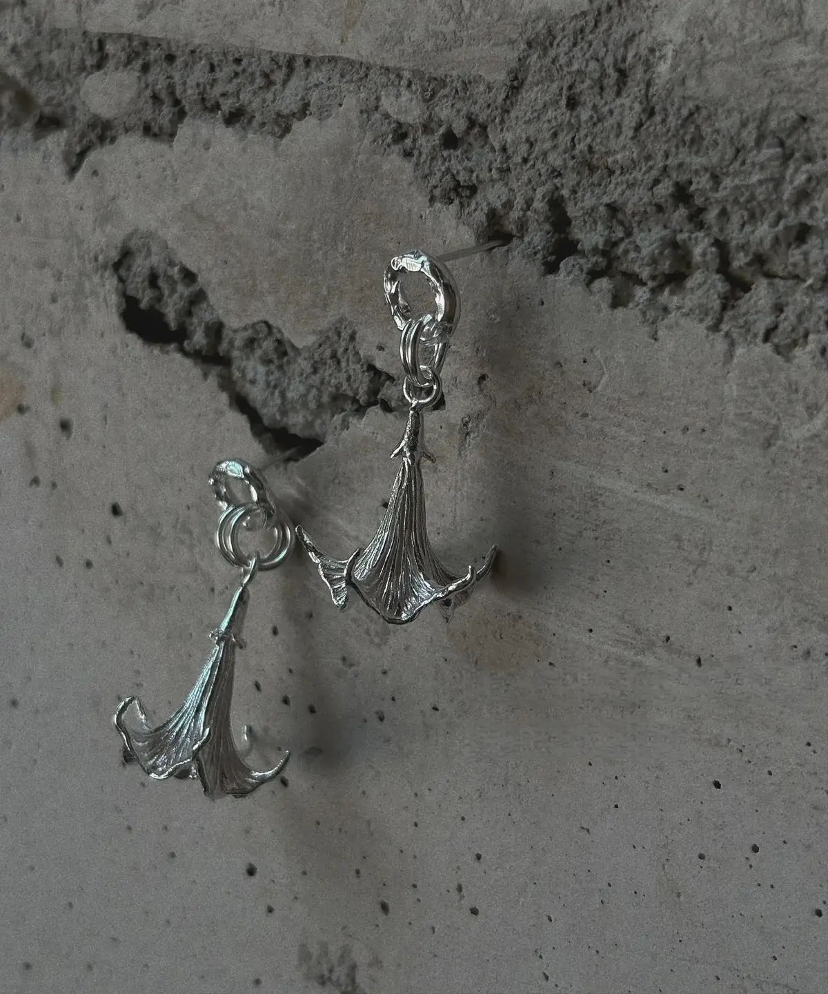 Datura-Handcrafted S925 Sterling Silver Flower Earrings 05 S925 Sterling Silver Datura Flower Earrings with sculptural, downward-facing blooms and textured petal details; handcrafted Silver Earrings styled against a rough concrete wall for contrast and elegance.