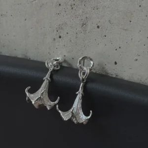S925 Sterling Silver Datura Flower Earrings with trumpet-shaped bloom and textured petals; handcrafted Silver Earrings styled on black surface with concrete backdrop, showcasing botanical elegance and artisanal detail.