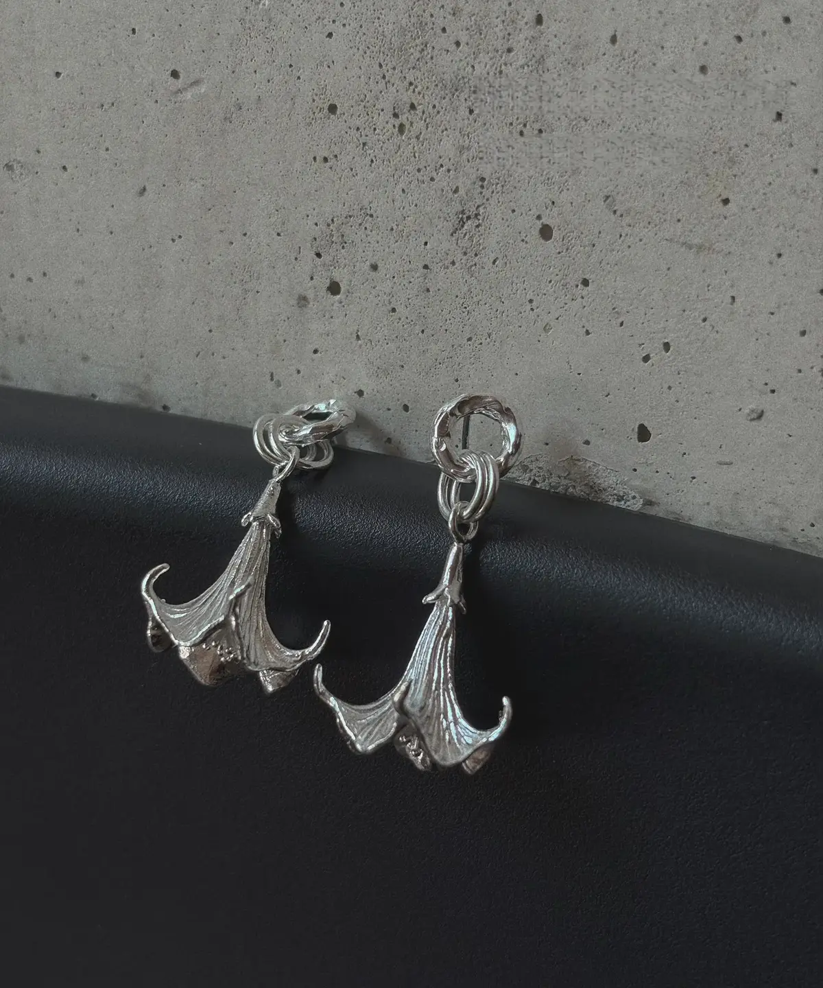 Datura-Handcrafted S925 Sterling Silver Flower Earrings 07 S925 Sterling Silver Datura Flower Earrings with trumpet-shaped bloom and textured petals; handcrafted Silver Earrings styled on black surface with concrete backdrop, showcasing botanical elegance and artisanal detail.