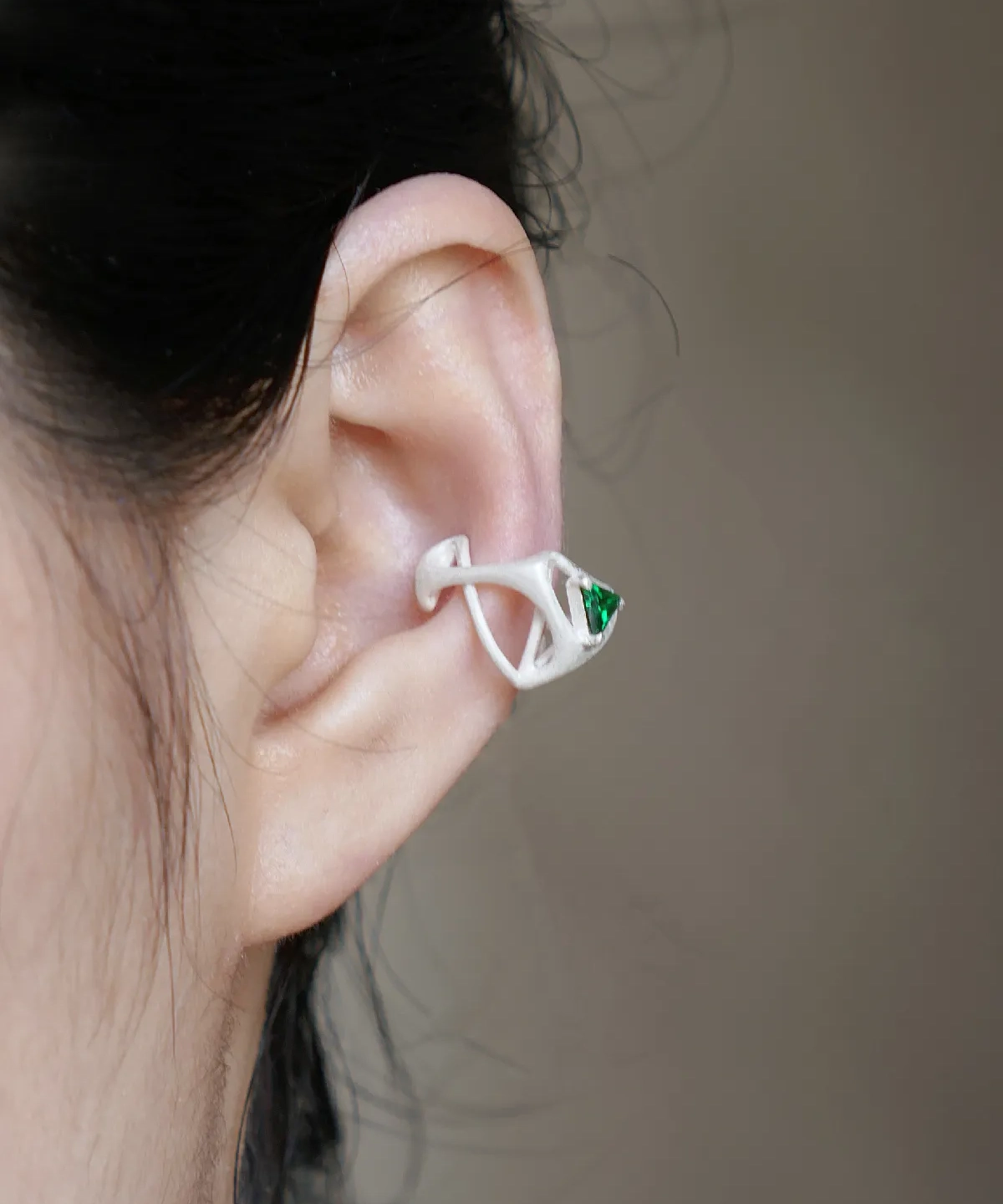 Close-up of ear wearing Dreamscape Garden S925 Silver Ear Cuff with green triangular gemstone and sculptural silver design; a modern Silver Ear Cuff blending botanical inspiration and geometric elegance.