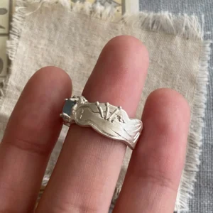 Hand wearing a Handmade 999 Silver Ring with sculptural reclining figure and a small Aquamarine gemstone; artistic design evokes mythic elegance and celebrates the March birthstone in finely crafted 999 Silver Ring detail.