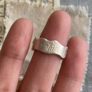 Hand wearing a Handmade 999 Silver Ring with engraved butterfly, floral, and sunburst motifs, featuring a light blue Aquamarine gemstone; a poetic Aquamarine Ring crafted in fine silver, celebrating March birthstone elegance and nature-inspired artistry.